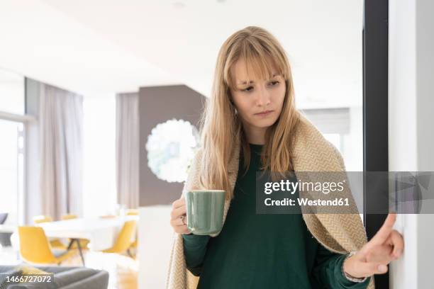 blond woman with tea cup adjusting thermostat at home - termostato foto e immagini stock