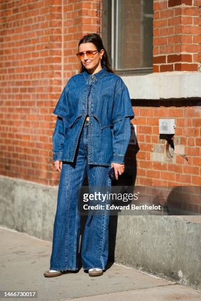 Guest wears orange sunglasses, a navy blue short sleeves cropped shirt, a matching navy blue denim shirt, matching navy blue denim large pants, white...