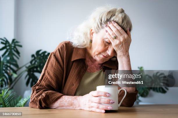 upset senior woman with head in hand sitting at home - com as mãos na cabeça imagens e fotografias de stock