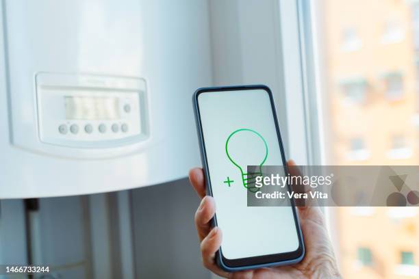 cropped view of woman hands holding screen phone with green sustainable energy water heater - boiler stockfoto's en -beelden