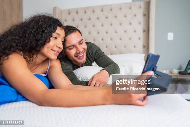 latin couple are lying on their bed with their tablet watching a movie while spending time together - free download photo stock pictures, royalty-free photos & images