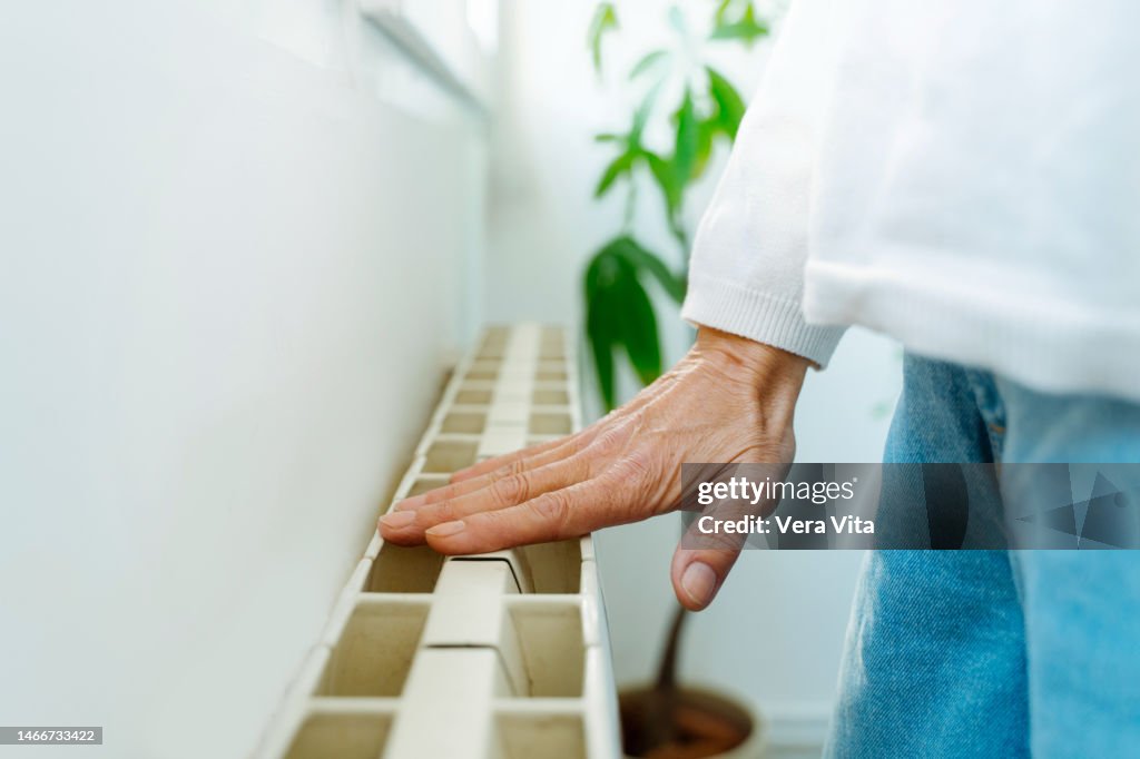 Cropped mature woman hand touching home radiator temperature with casual clothes