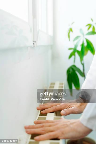 cropped mature woman hand touching white home radiator temperature - vita domestica fotografías e imágenes de stock