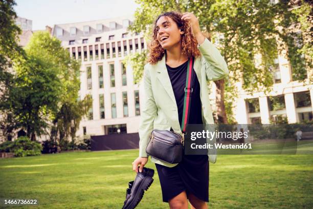 happy businesswoman holding shoes walking in office park - crossbody bag stock pictures, royalty-free photos & images