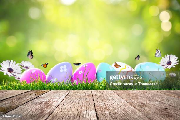 easter day, wooden table on a background with eggs in the lawn on a sunny day - easter background stock pictures, royalty-free photos & images