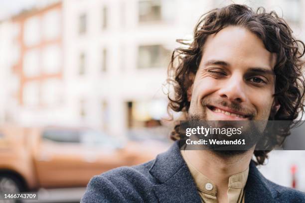 happy young businessman with curly hair winking - zwinkern stock-fotos und bilder