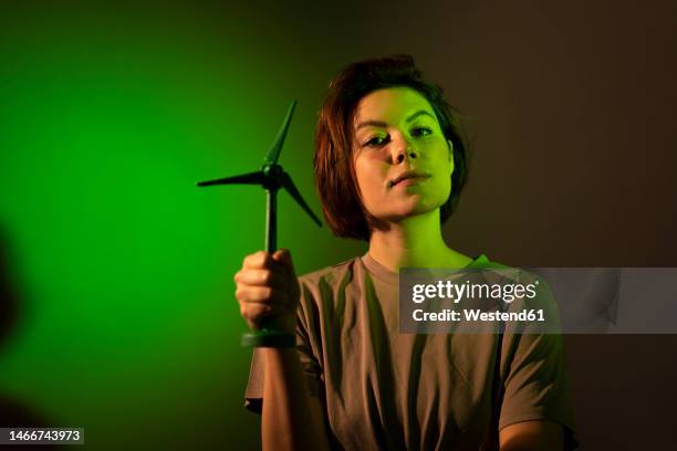 businesswoman with short hair holding wind turbine model against colored background - exigir - fotografias e filmes do acervo