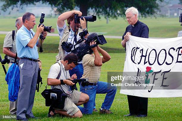 Members of the news media photograph Father Fred Ruse of Winter Haven, Florida, holding a banner reading "Choose Life" before the execution of Aileen...