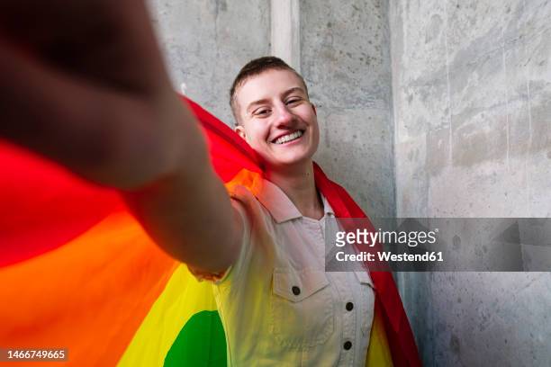 cheerful non-binary person taking selfie with rainbow flag - lgbtqi stock pictures, royalty-free photos & images