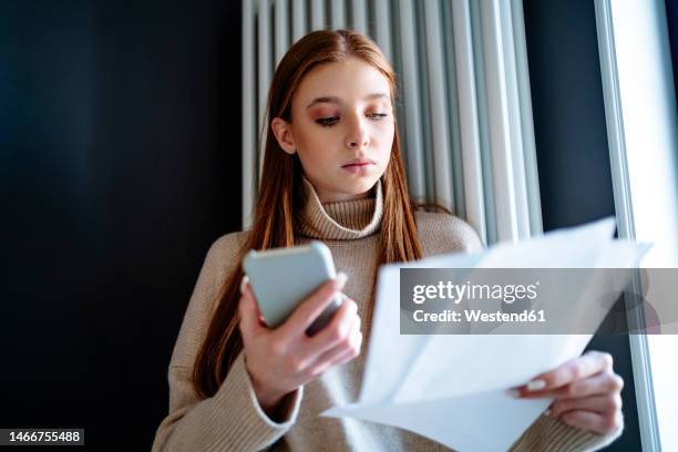 teenage girl looking at energy bill standing by radiator heater - energy bill stock pictures, royalty-free photos & images