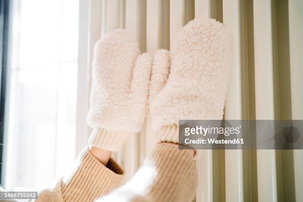 hands of teenage girl with mittens touching on radiator heater - woman hands in mittens stock-fotos und bilder