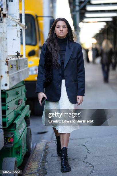 Guest wears diamonds earrings, a black turtleneck t-shirt, a black blazer jacket, a white tweed midi skirt, black shiny leather laces ankle boots ,...