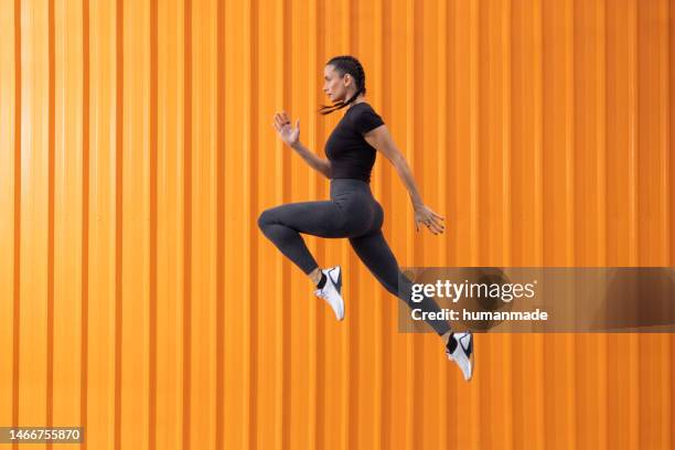 mujer bonita en forma saltando frente al fondo naranja - salto alto fotografías e imágenes de stock