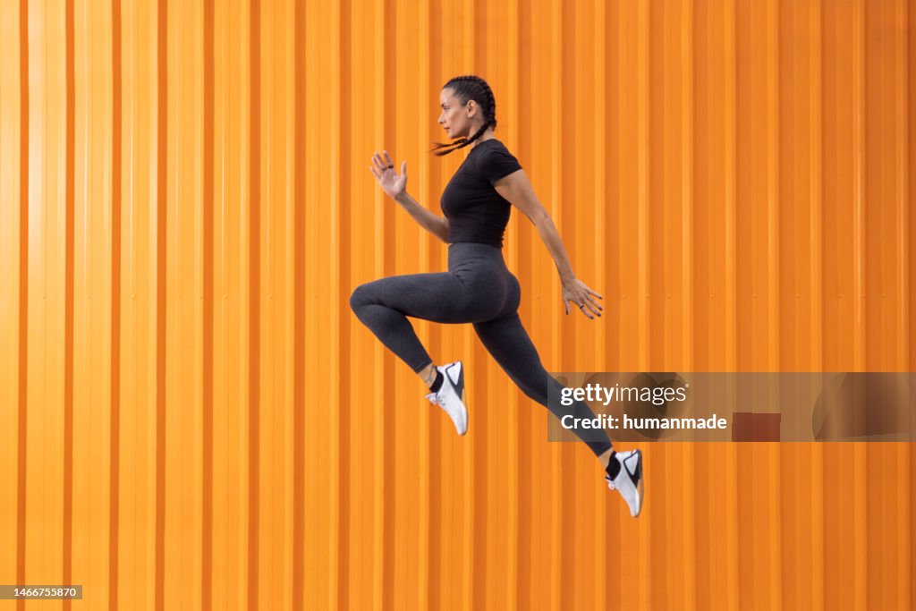 Fit pretty woman jumping in front of the orange background