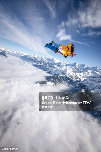 wingsuit flier sails high above the mountains in winter - wing suit stock pictures, royalty-free photos & images