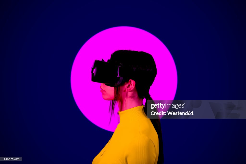 Young woman wearing VR Goggles by pink circle on black background