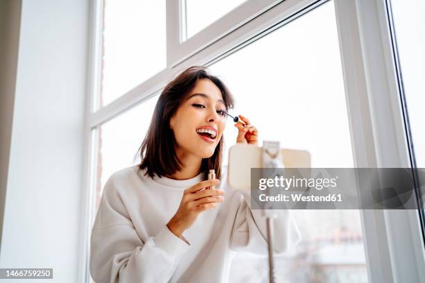 happy influencer filming make-up tutorial through smart phone - mascara stockfoto's en -beelden