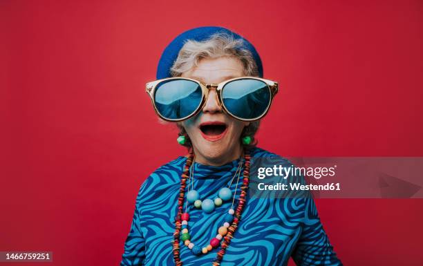 surprised senior woman wearing big sunglasses against red background - big sunglasses stock pictures, royalty-free photos & images