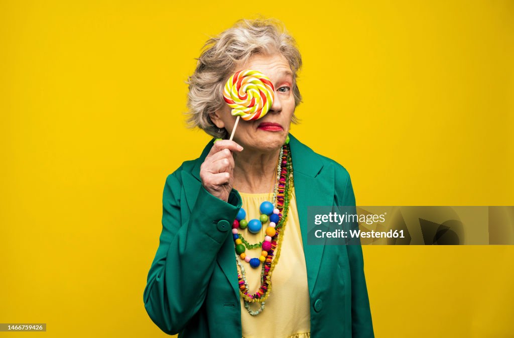 Woman covering eye with spiral candy against yellow background