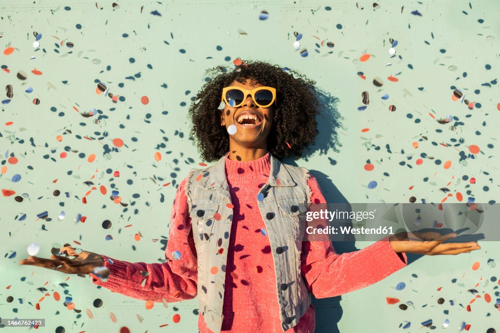 Cheerful woman with confetti enjoying in front of green wall