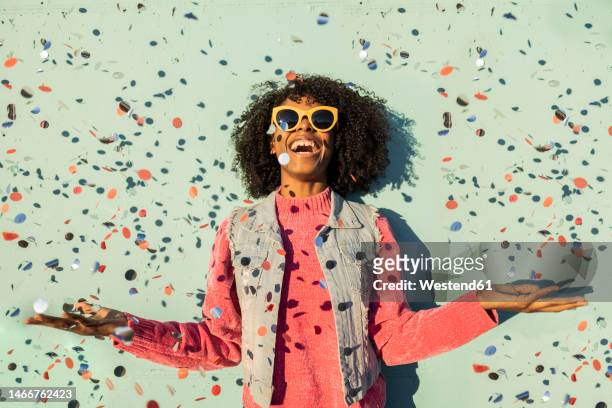 cheerful woman with confetti enjoying in front of green wall - celebration photos et images de collection