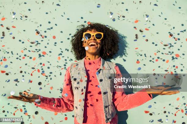 cheerful woman with confetti enjoying in front of green wall - celebration foto e immagini stock