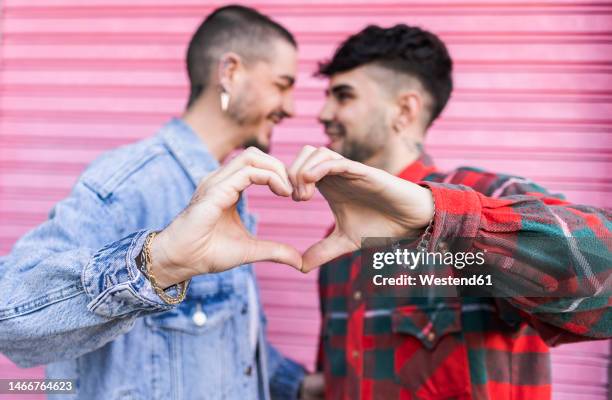 gay couple gesturing heart shape in front of pink roller shutter - two hearts stock-fotos und bilder