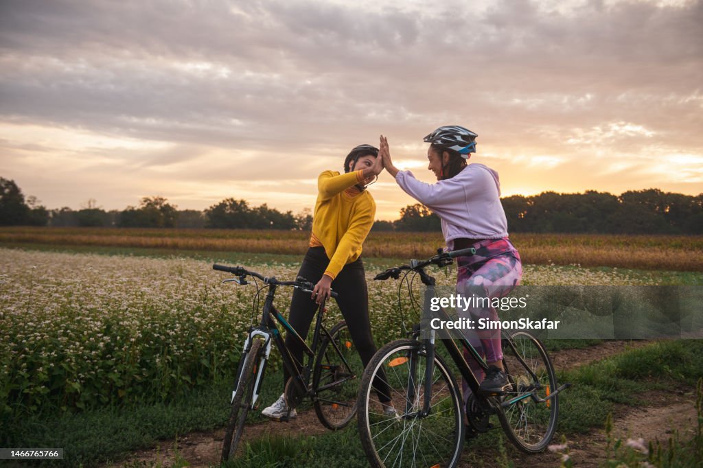 Athletes giving high five while riding bicycles on dirt road