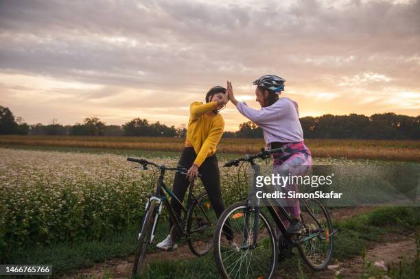athletes giving high five while riding bicycles on dirt road - bike winning imagens e fotografias de stock