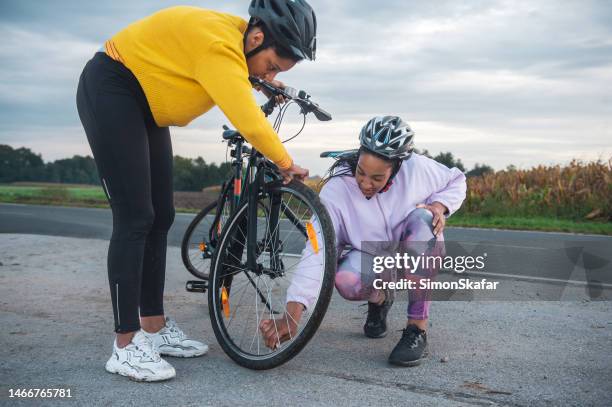 female friends fixing flat tire of bicycle on road - flat tyre stock pictures, royalty-free photos & images