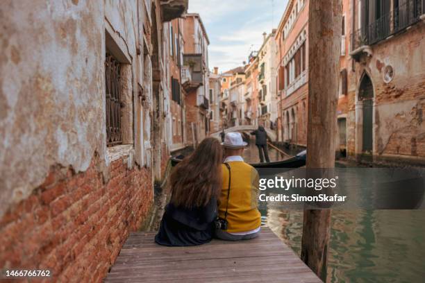 coppia che si siede sul molo tra gli edifici storici a venezia - venice couple foto e immagini stock