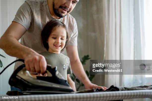 father and son ironing clothes at home - bügeln stock-fotos und bilder