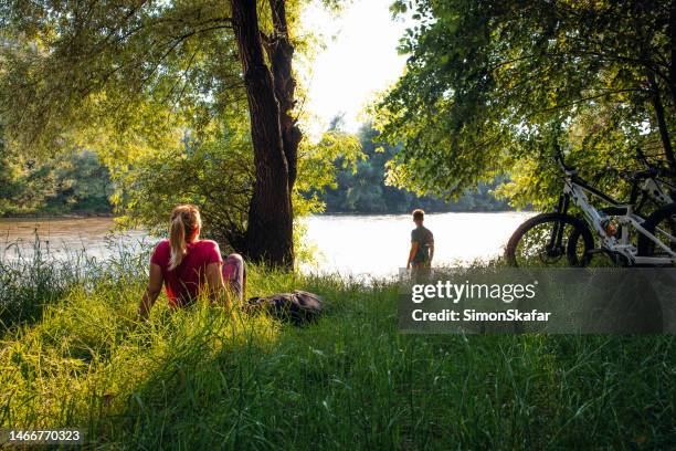 couple resting on river bank in forest - rivier gras oever stockfoto's en -beelden