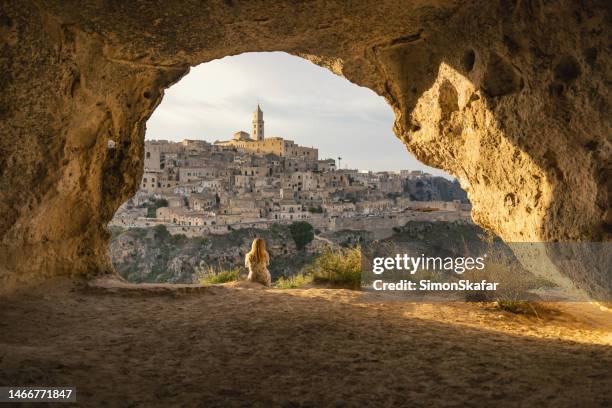 female tourist looking at cityscape while sitting at cave. matera - italy - matera stock pictures, royalty-free photos & images