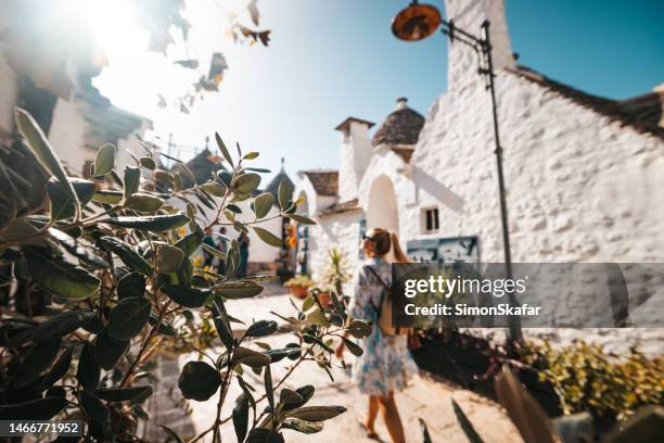 mittelerwachsene weibliche touristin mit rucksack, die trulli-häuser in der altstadt gegen klaren himmel in alberobello an sonnigen tagen erkundet - trulli stock-fotos und bilder