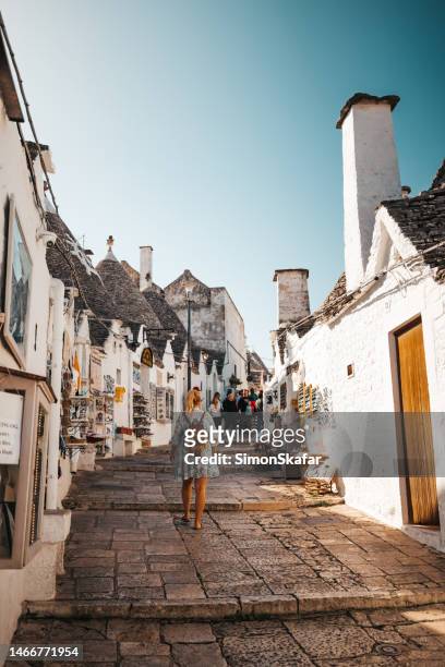 rear view of female tourist with backpack walking in alley amidst trulli houses against clear sky at alberobello - bari italy stockfoto's en -beelden