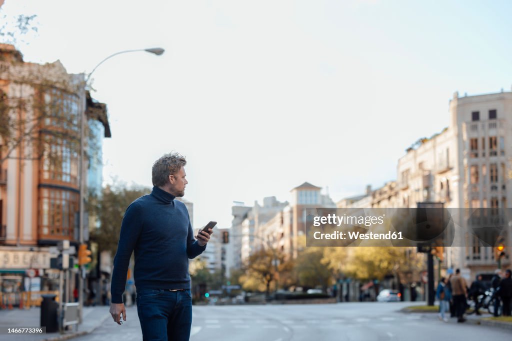 Man with mobile phone crossing road in city