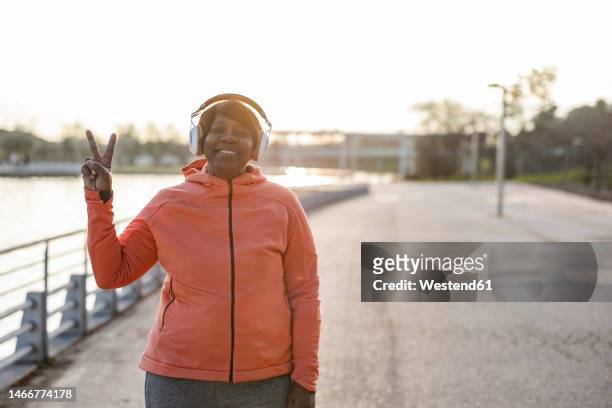 smiling senior woman wearing headphones showing peace sign at promenade - pensioners demonstrate in spain stock pictures, royalty-free photos & images
