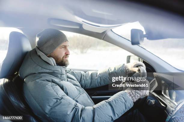 man wearing knit hat driving car - coat drive stock pictures, royalty-free photos & images