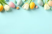 Happy Easter concept. Frame top border made of tulips spring flowers and colorful Easter eggs on light blue background.