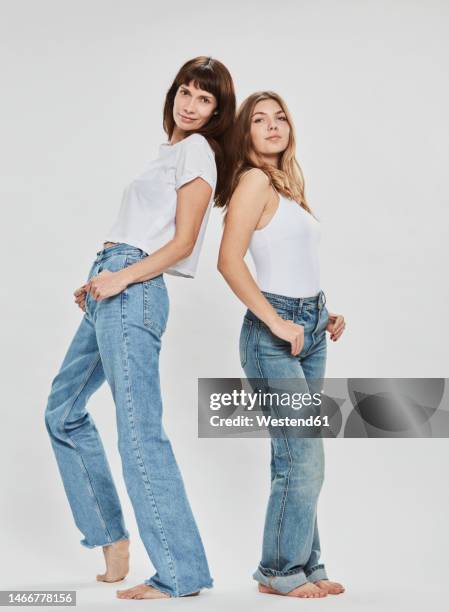 confident mother and daughter standing back to back against white background - adolescent daughter mother portrait stock-fotos und bilder