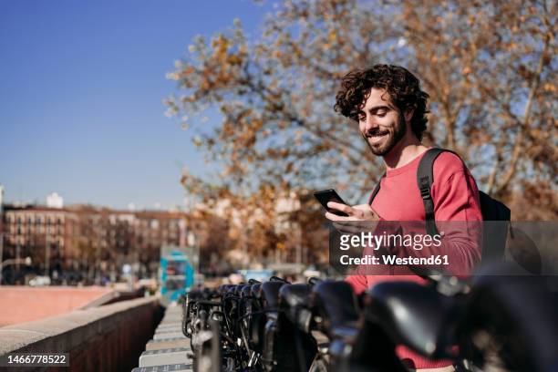 happy man using mobile app to rent electric push scooter on sunny day - mobile banking stock-fotos und bilder