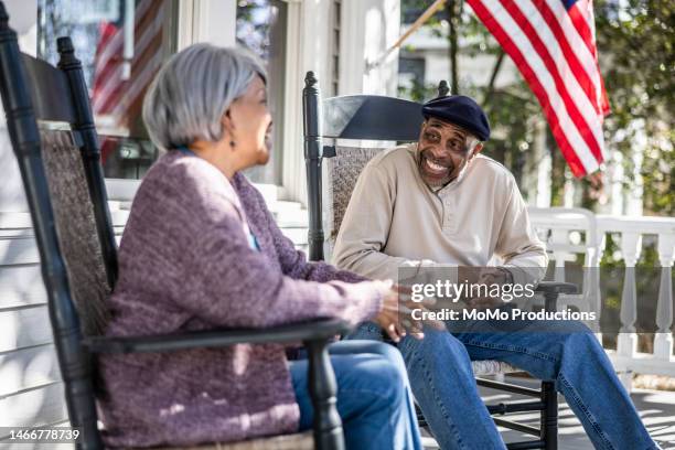 senior couple talking in rocking chairs on front porch - vlag plaatsen stockfoto's en -beelden