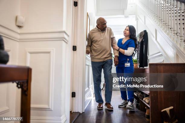 in-home nurse helping senior man walk through his hallway - differing abilities fotografías e imágenes de stock