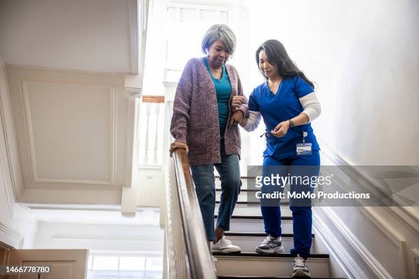in-home nurse helping senior woman down a staircase - mobility disability stock pictures, royalty-free photos & images