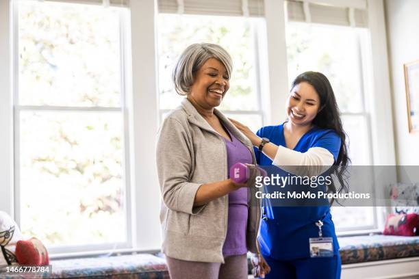at home nurse helping senior woman with physical therapy at home - pflegedienst blau stock-fotos und bilder