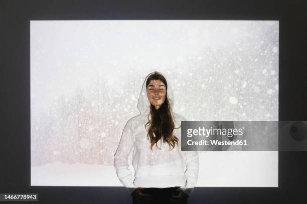 happy woman with eyes closed standing in front of snowfall on projection screen - person standing infront of wall stockfoto's en -beelden