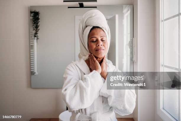 smiling mature woman massaging face in bathroom at home - accappatoio foto e immagini stock