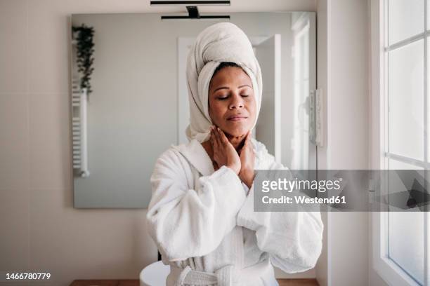 smiling mature woman massaging face in bathroom at home - woman bathrobe stock pictures, royalty-free photos & images