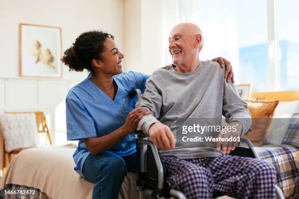 happy nurse with senior man sitting on wheelchair in bedroom at home - nursing homes ストックフォトと画像